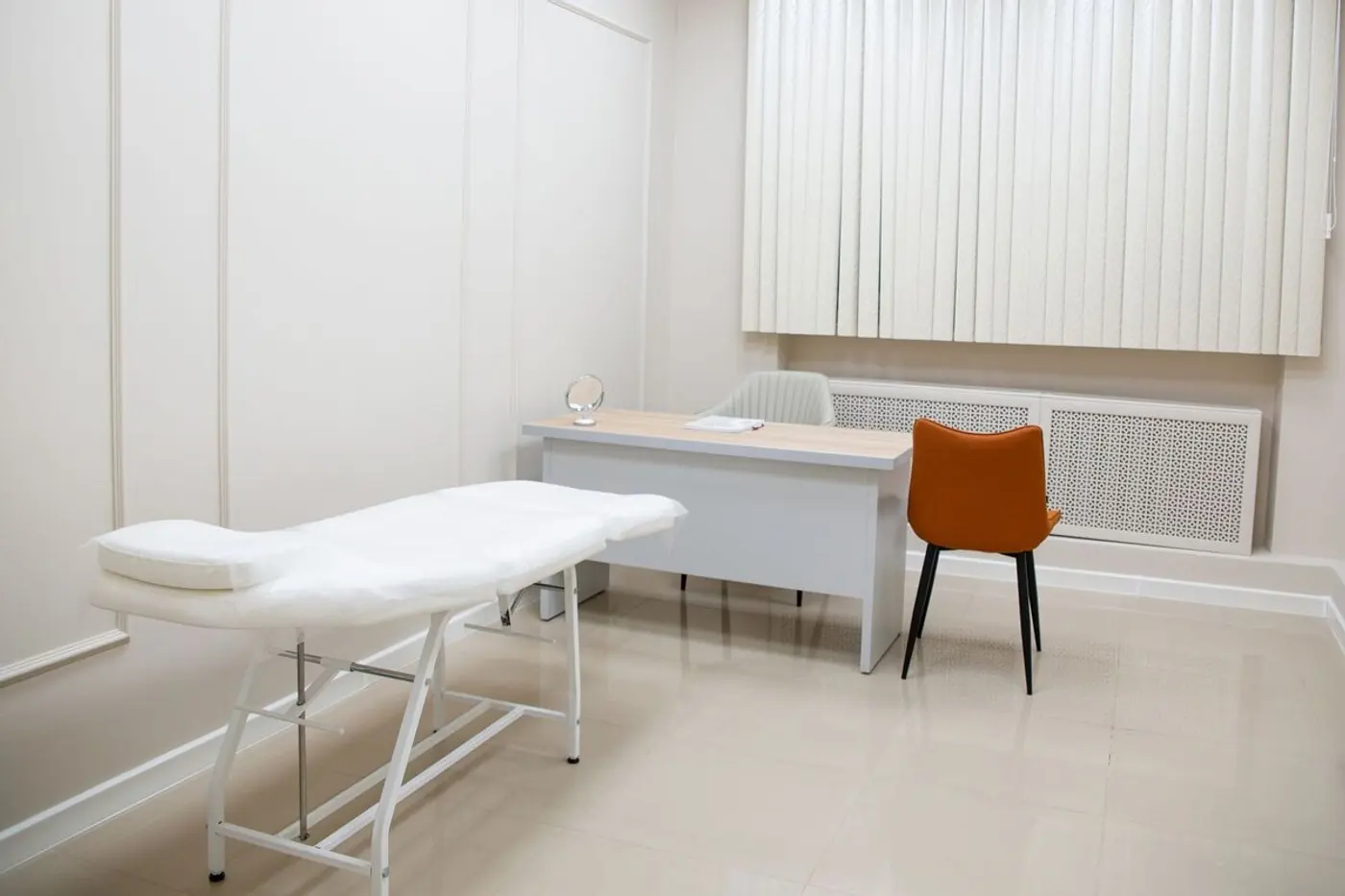 A bright, tidy clinic exam room with an examination table and desk