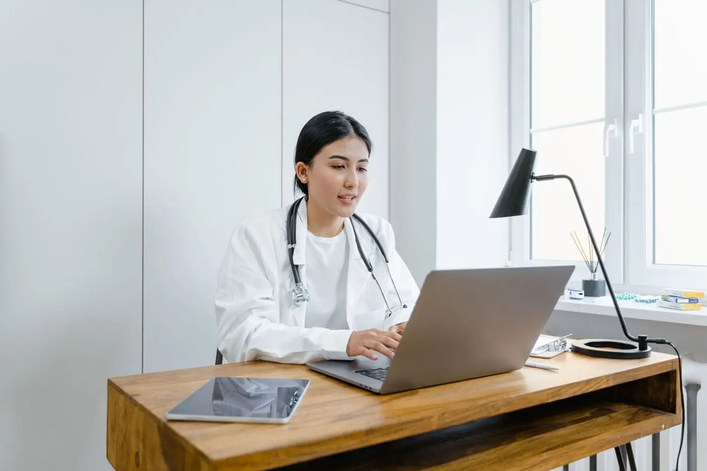 A physician works at a laptop in a bright clinic office