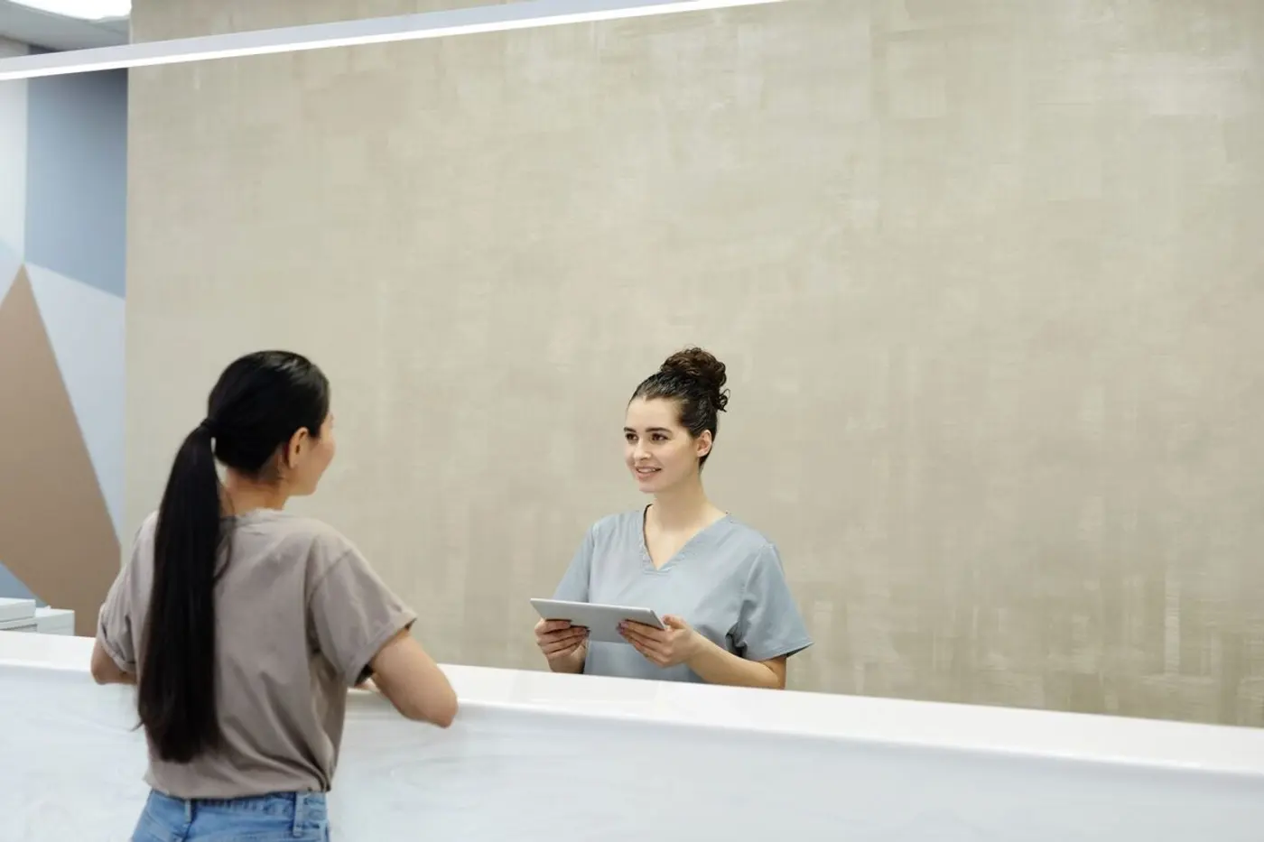 A clinic receptionist speaks with a visitor at the front desk