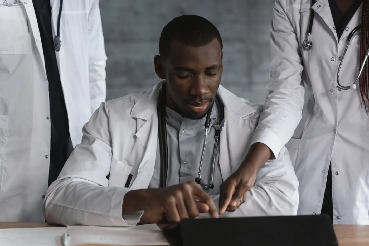 Three clinicians in white coats review a tablet together